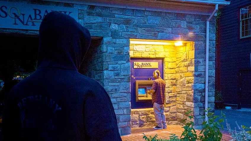 crook looms over man at ATM